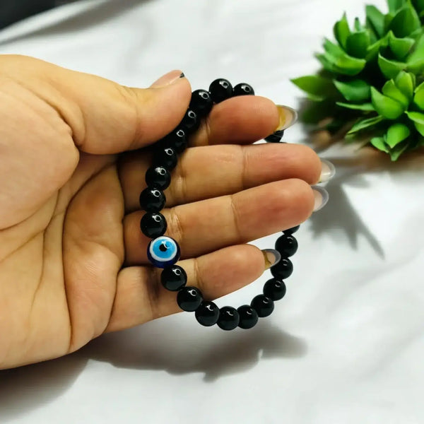 A stylish black obsidian bracelet with a prominent blue evil eye charm, held in a hand.