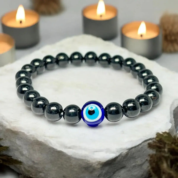 A bracelet crafted with dark glossy beads, featuring a prominent blue and white evil eye charm in the center, displayed on a white stone surface.
