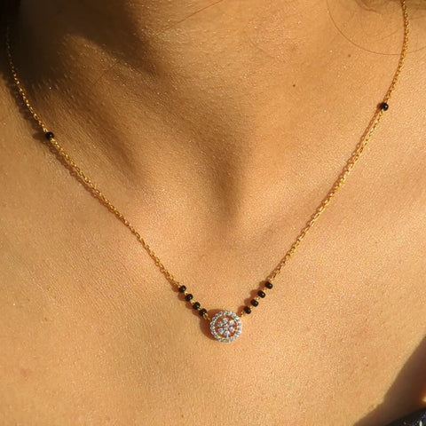 A close-up image of a 92.5 sterling silver mangalsutra with a gold plated short chain, showcasing a circular pendant embellished with shimmering cubic zirconia stones, against a warm, skin-toned background.