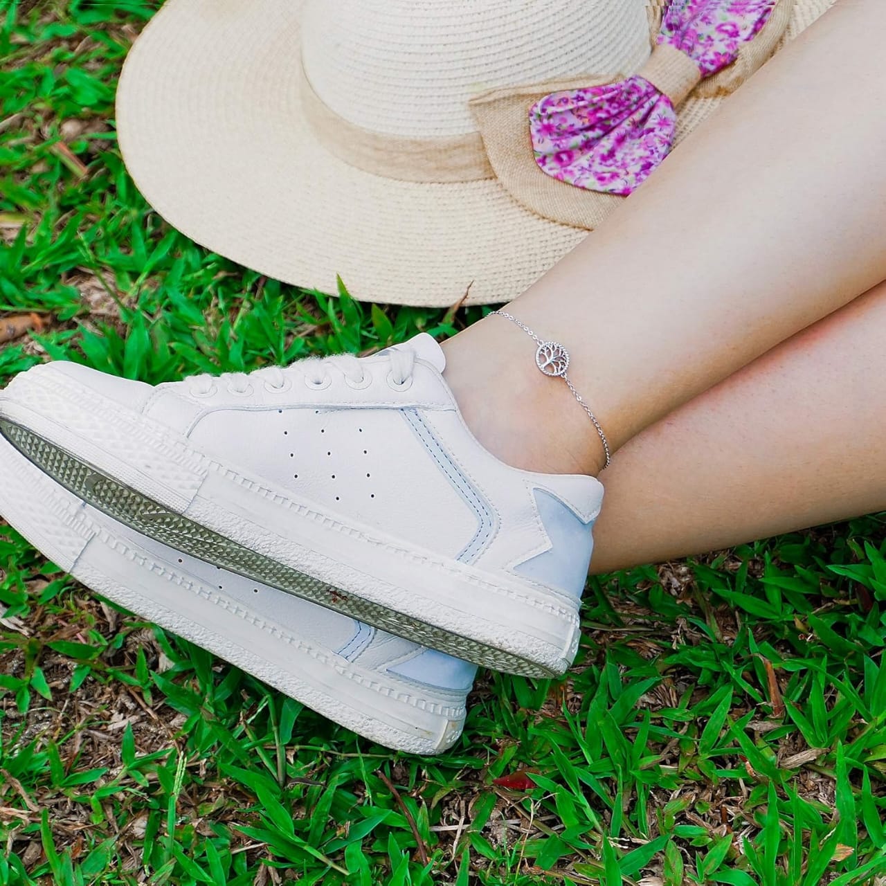 Lifestyle photo of the sterling silver Tree of Life anklet worn with white platform sneakers on green grass.
