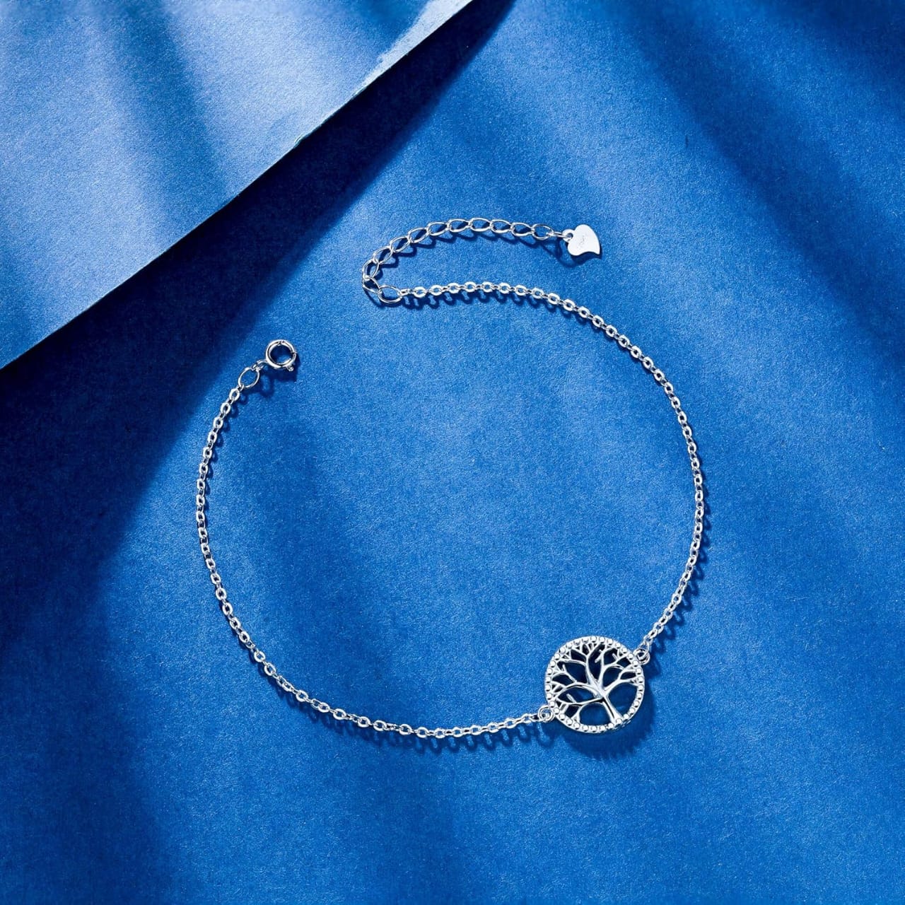 High-polish sterling silver anklet featuring a detailed Tree of Life symbol, styled on a blue textured background.
