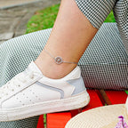 White sneaker with gray accents worn by a person sitting on a red bench, wearing a silver anklet with a tree charm.